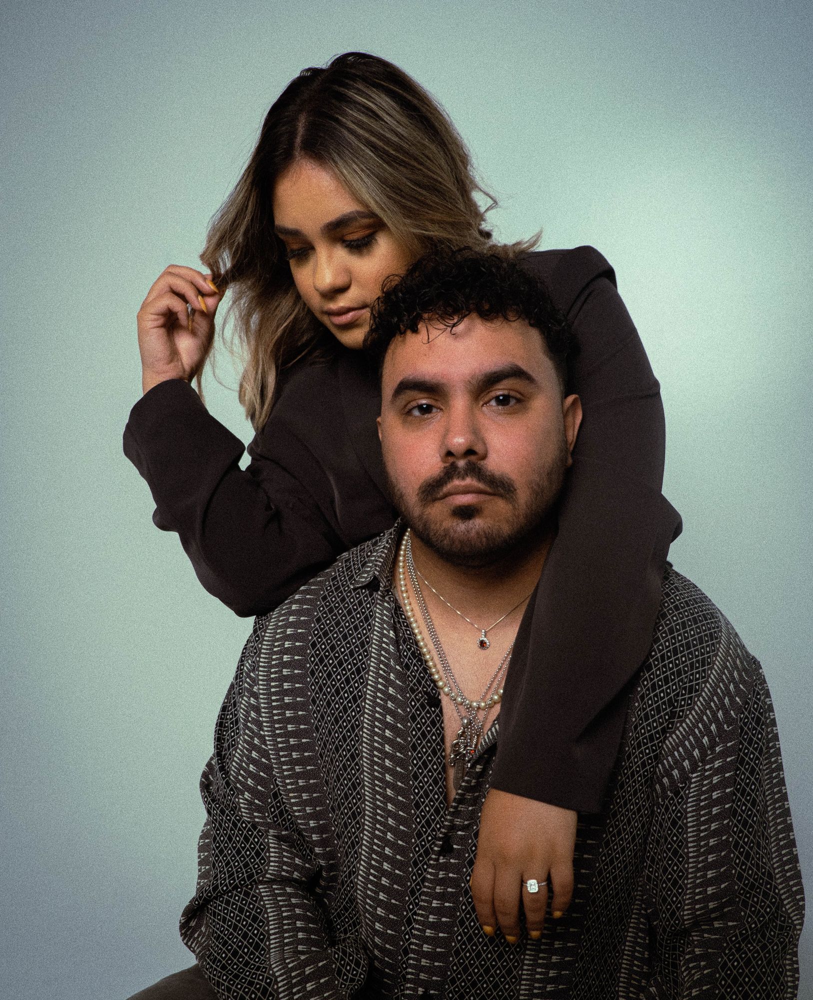 Engaged couple in the studio, her hand with the engagement ring resting on his chest