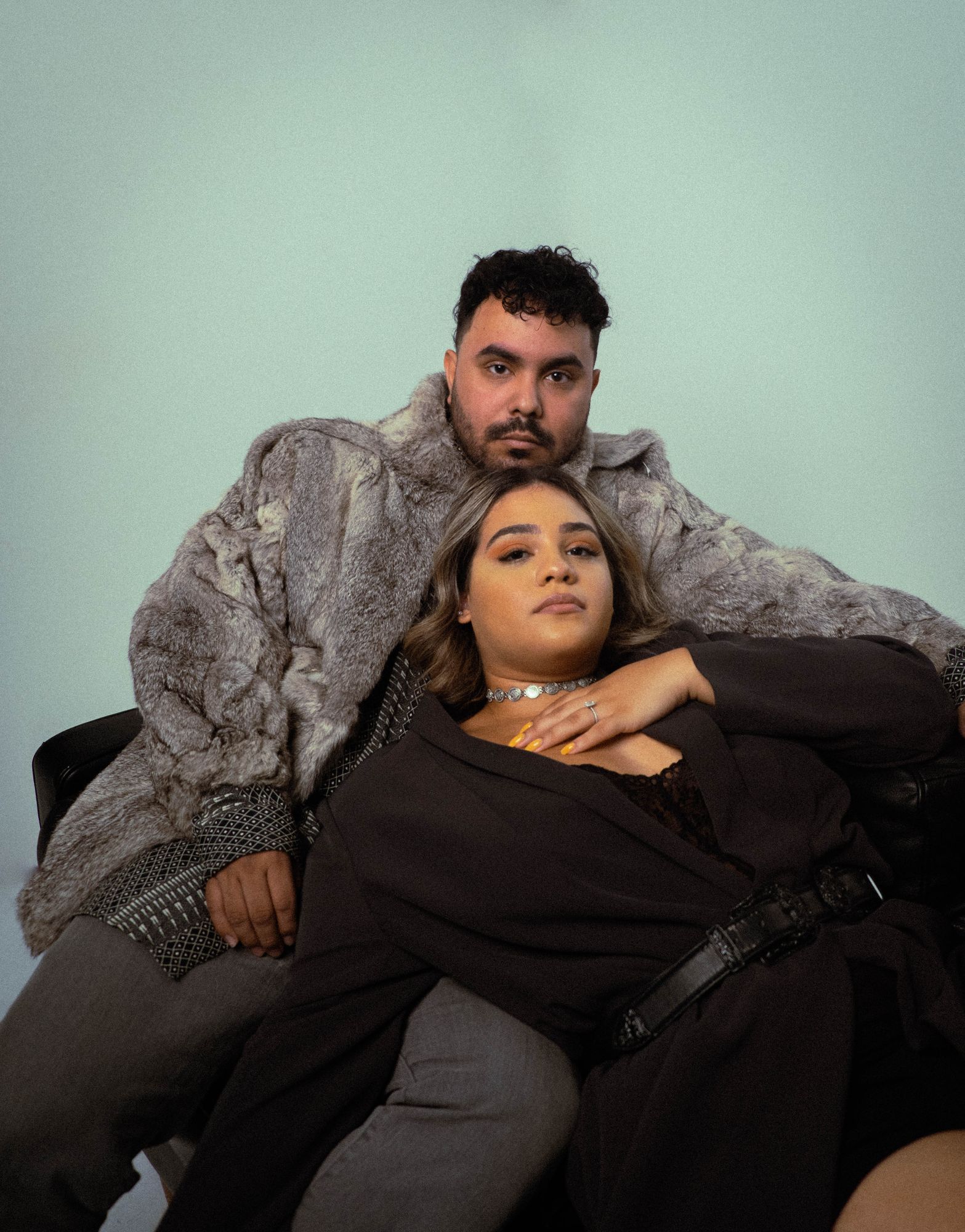 Engaged couple seated together, she leans back against him in a fur coat