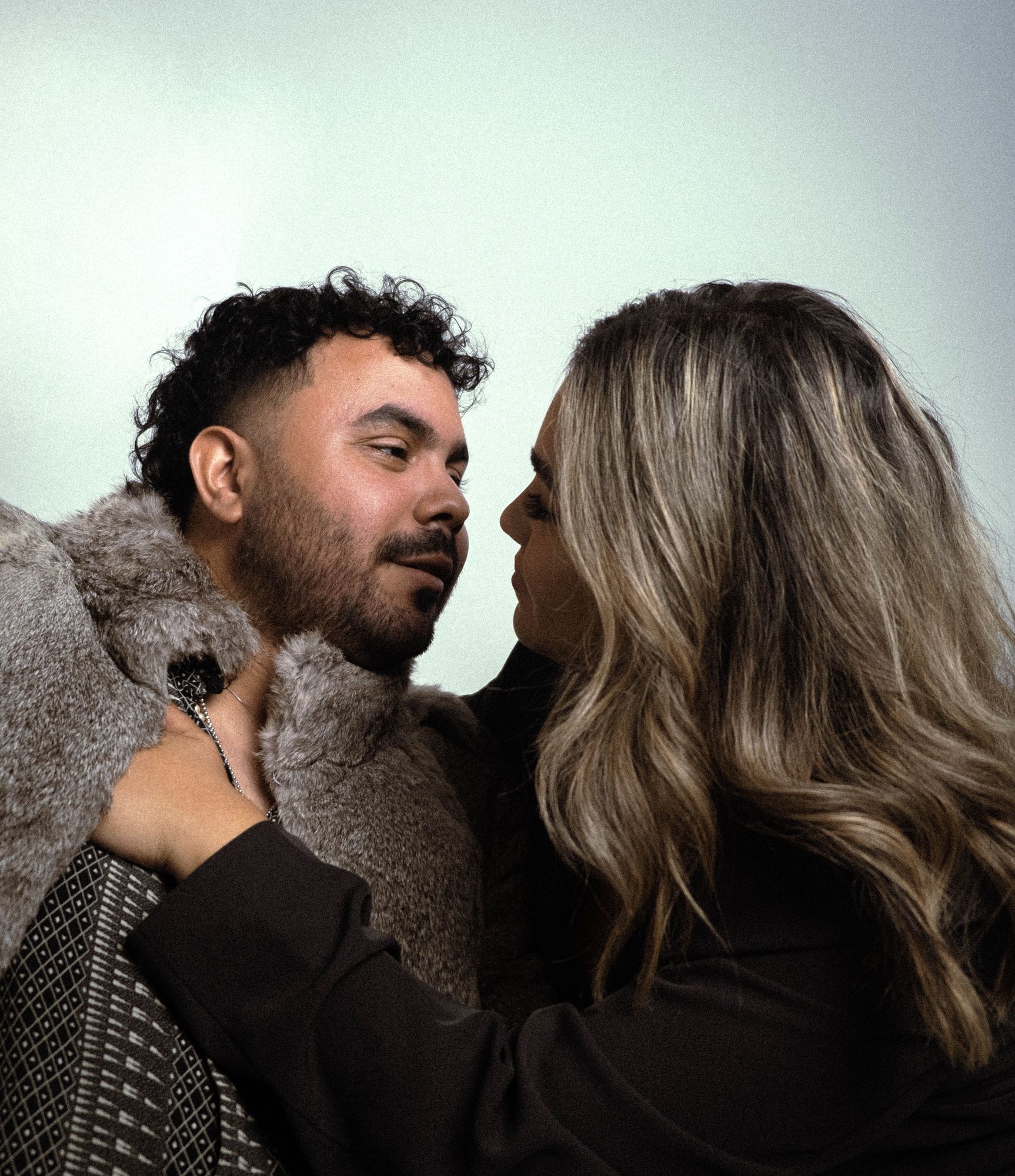 Engaged couple face to face, about to kiss, on a sage backdrop