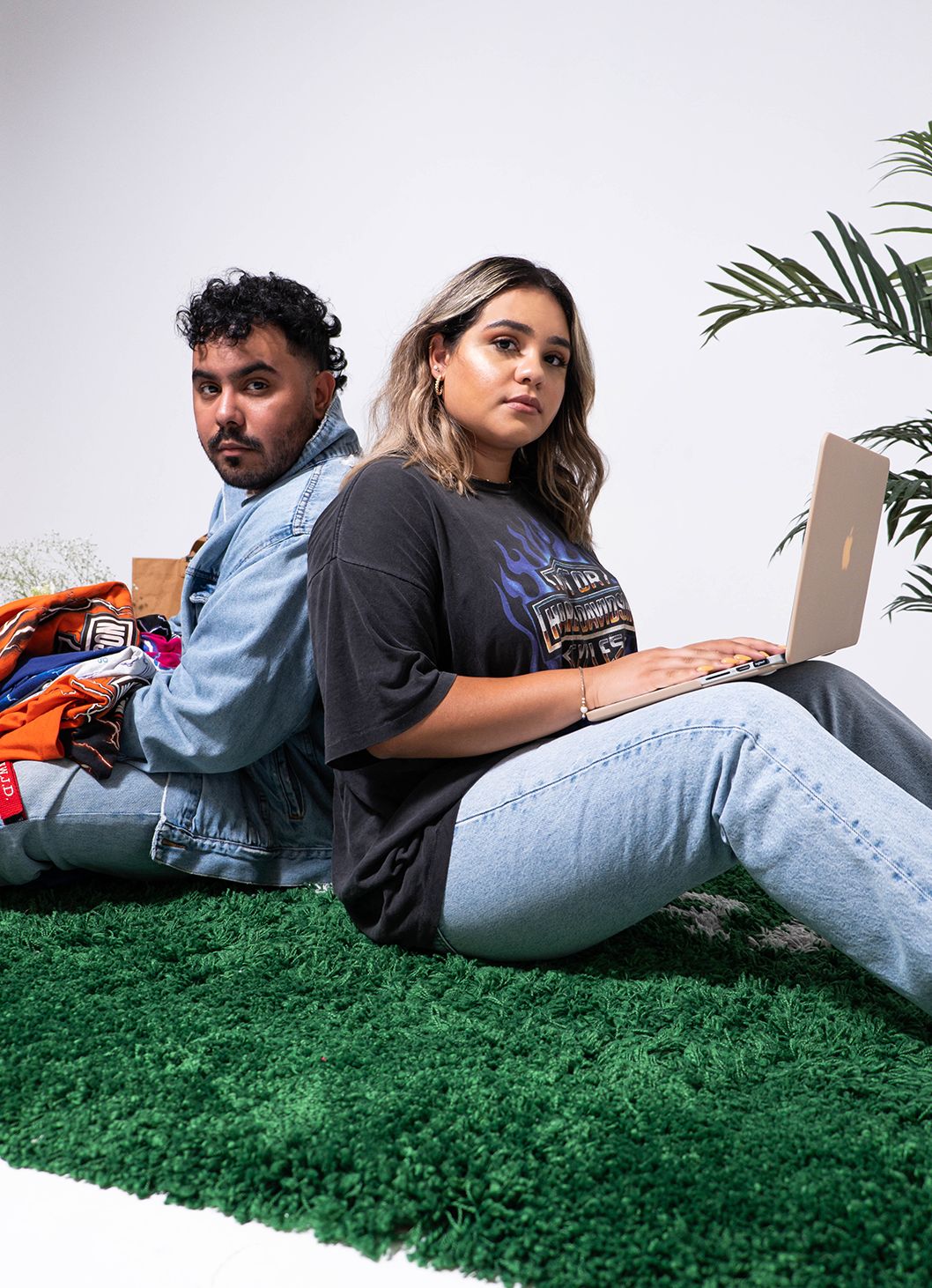 Engaged couple sitting back to back on a green rug in a white studio set